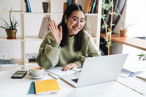 A person smiling and waving at her laptop screen
